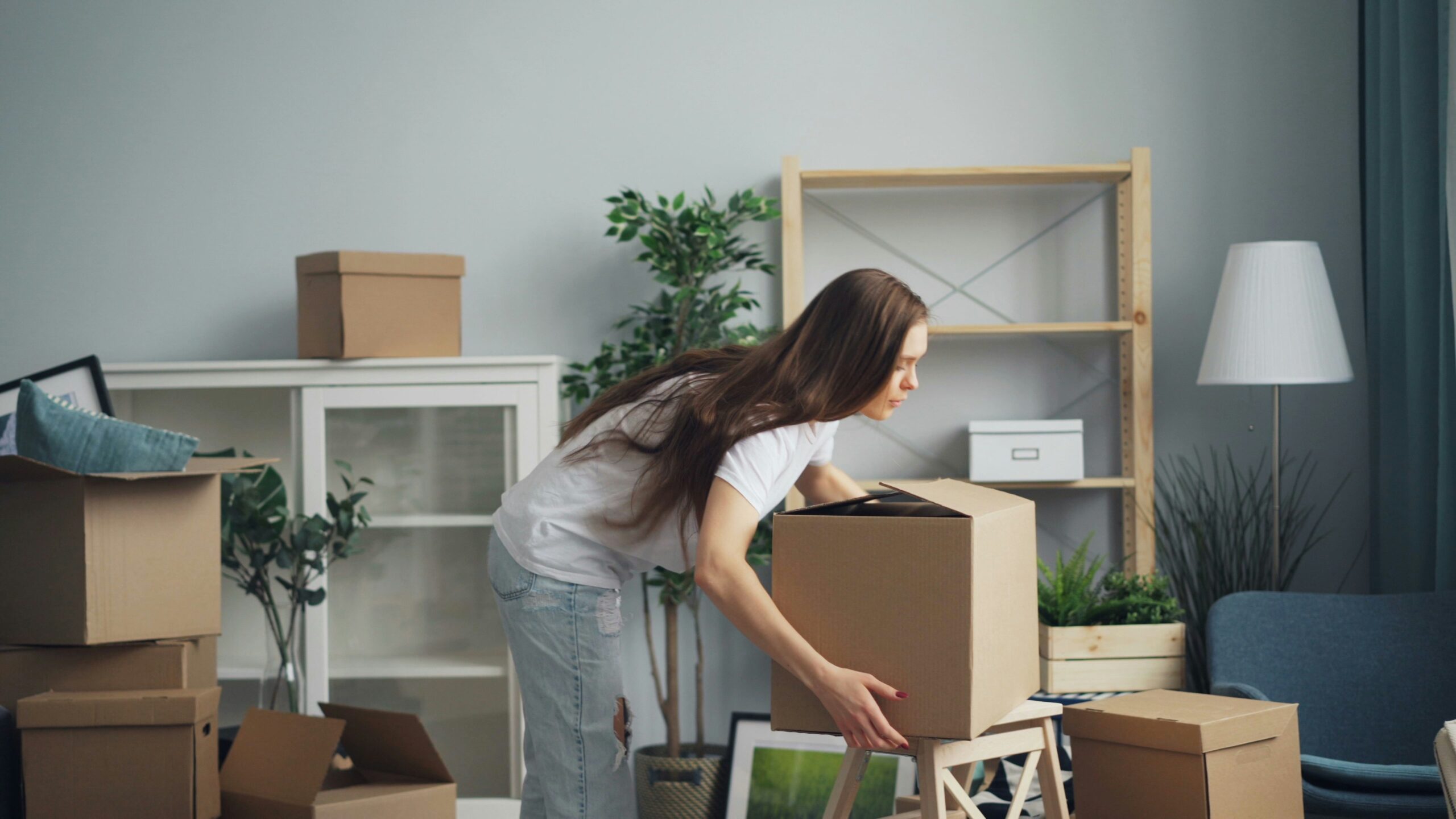 Woman packing belongings into cardboard boxes in a modern living space, illustrating the moving process and the convenience of packing solutions for relocations.