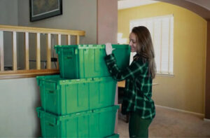 Person packing items into eco-friendly plastic bins indoors, highlighting sustainable moving solutions for winter